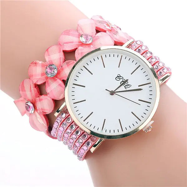 A pink women's watch featuring a floral crystal charm bracelet band and a clean white analog watch face.