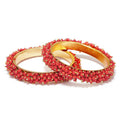 A set of gold-polished brass bangles decorated with vibrant red beads.