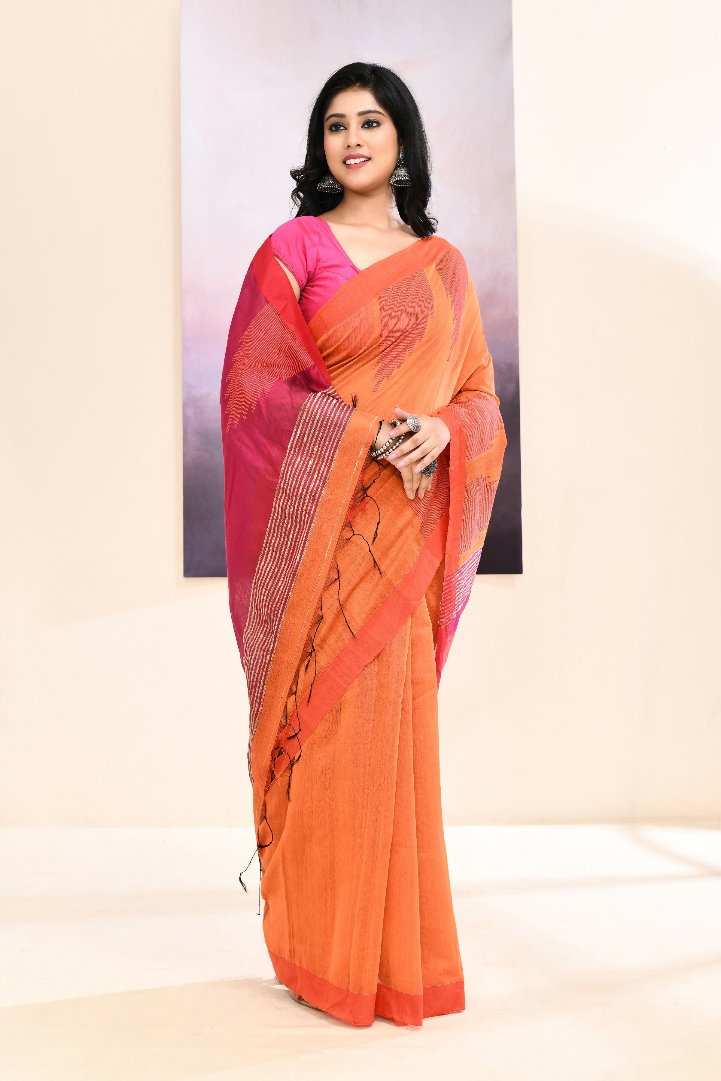 Vibrant orange cotton blend Jamdani saree featuring a traditional temple border and detailed embellishments.