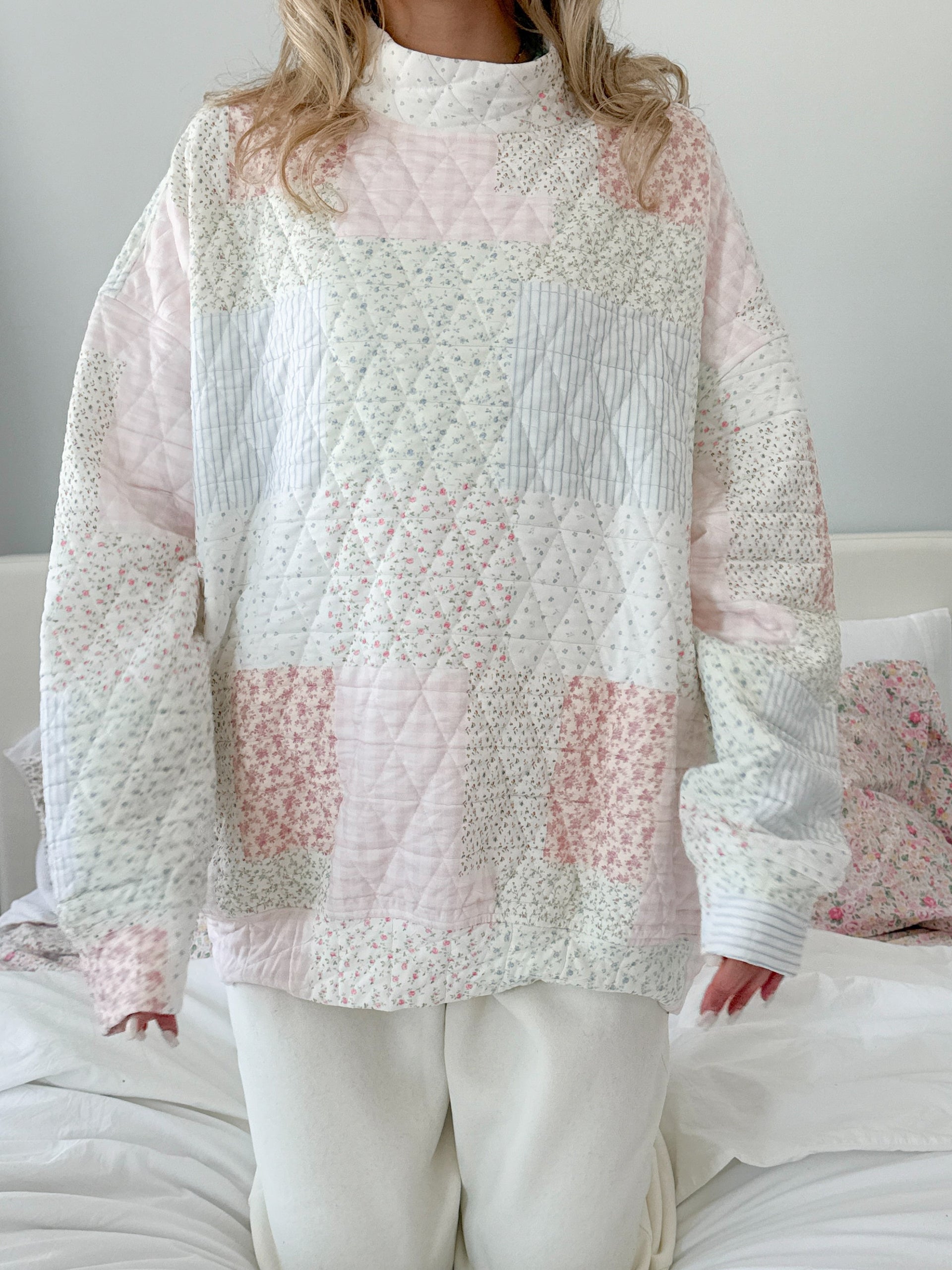 Model wearing an oversized quilted pastel mockneck sweatshirt with floral and striped patchwork patterns