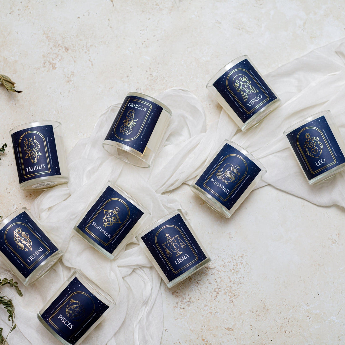 A collection of navy blue glass candles with gold zodiac signs including Taurus, Scorpio, Virgo, Leo, Gemini, Sagittarius, Libra, and Pisces.