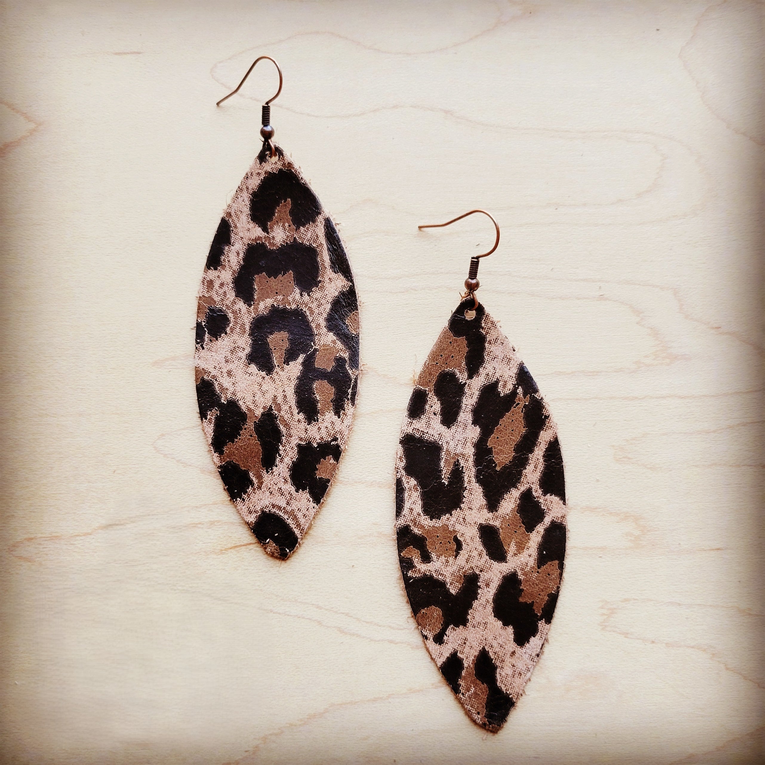 A pair of narrow oval-shaped suede leather earrings featuring a brown and black leopard print pattern.