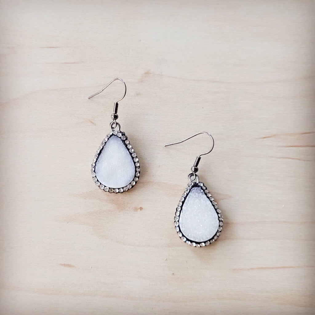 A pair of sparkling white druzy teardrop earrings with silver-tone trim on a wooden background
