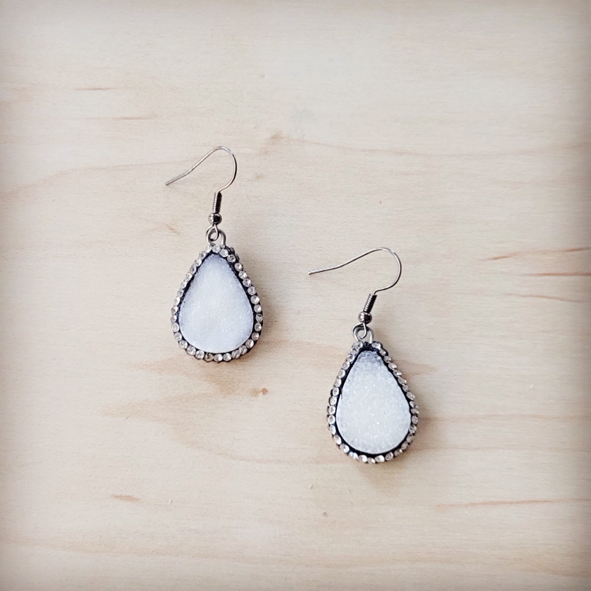 A pair of sparkling white druzy teardrop earrings with silver-tone trim on a wooden background
