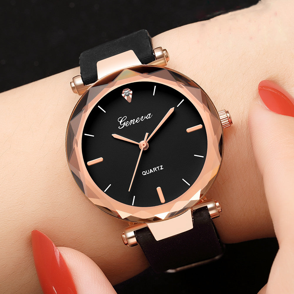 Close up of a women's round watch with a black face, rose gold bezel, and black silicone strap worn on a wrist.