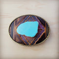 Oval leather belt buckle with magenta geometric inlay, blue turquoise stone center, and brass rope edge detail.