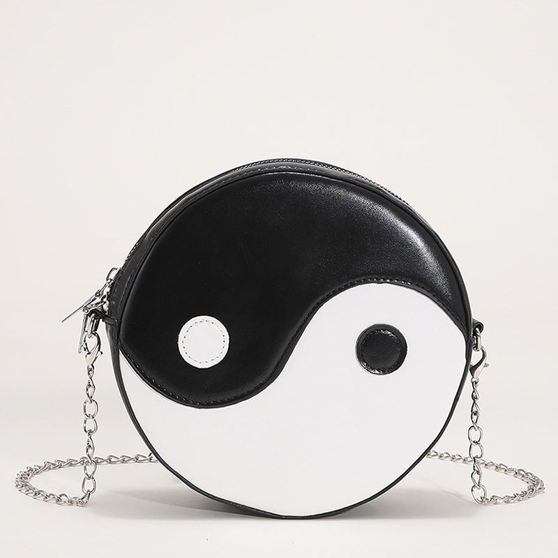 Black and white Yin Yang round crossbody messenger bag with a silver chain strap, shown on a clean background and being held by a hand.