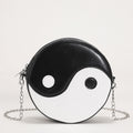 Black and white Yin Yang round crossbody messenger bag with a silver chain strap, shown on a clean background and being held by a hand.