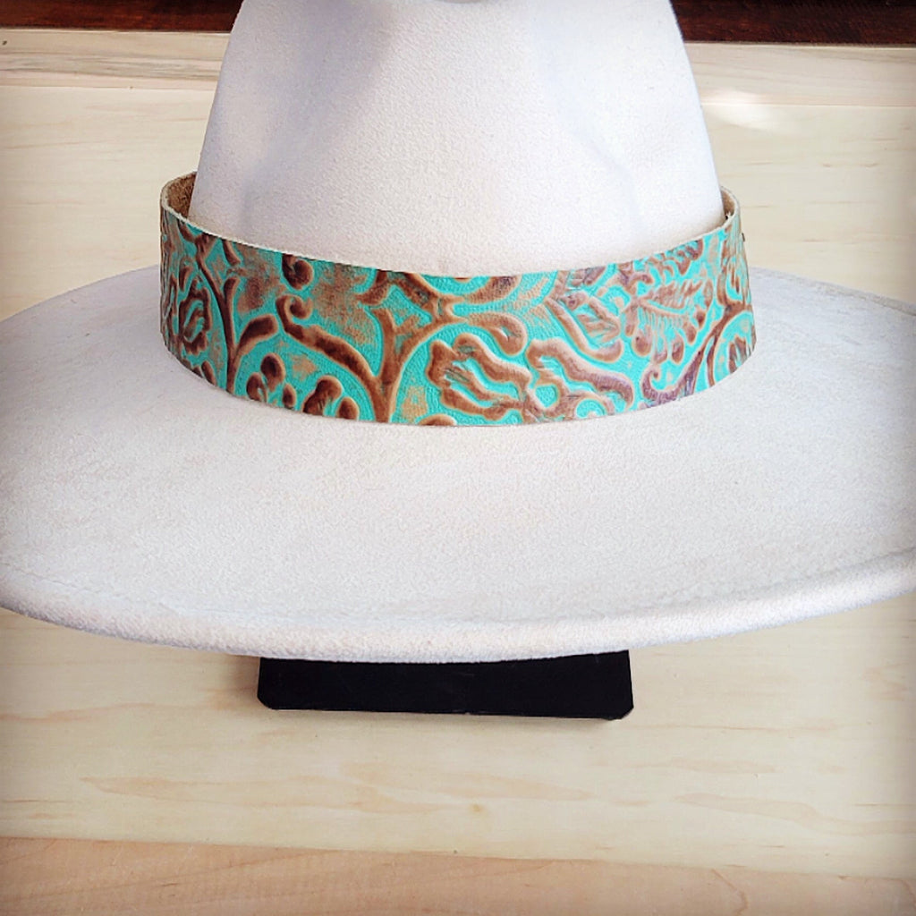 A wide, turquoise and brown floral tooled leather hat band wrapped around a white cowboy hat.