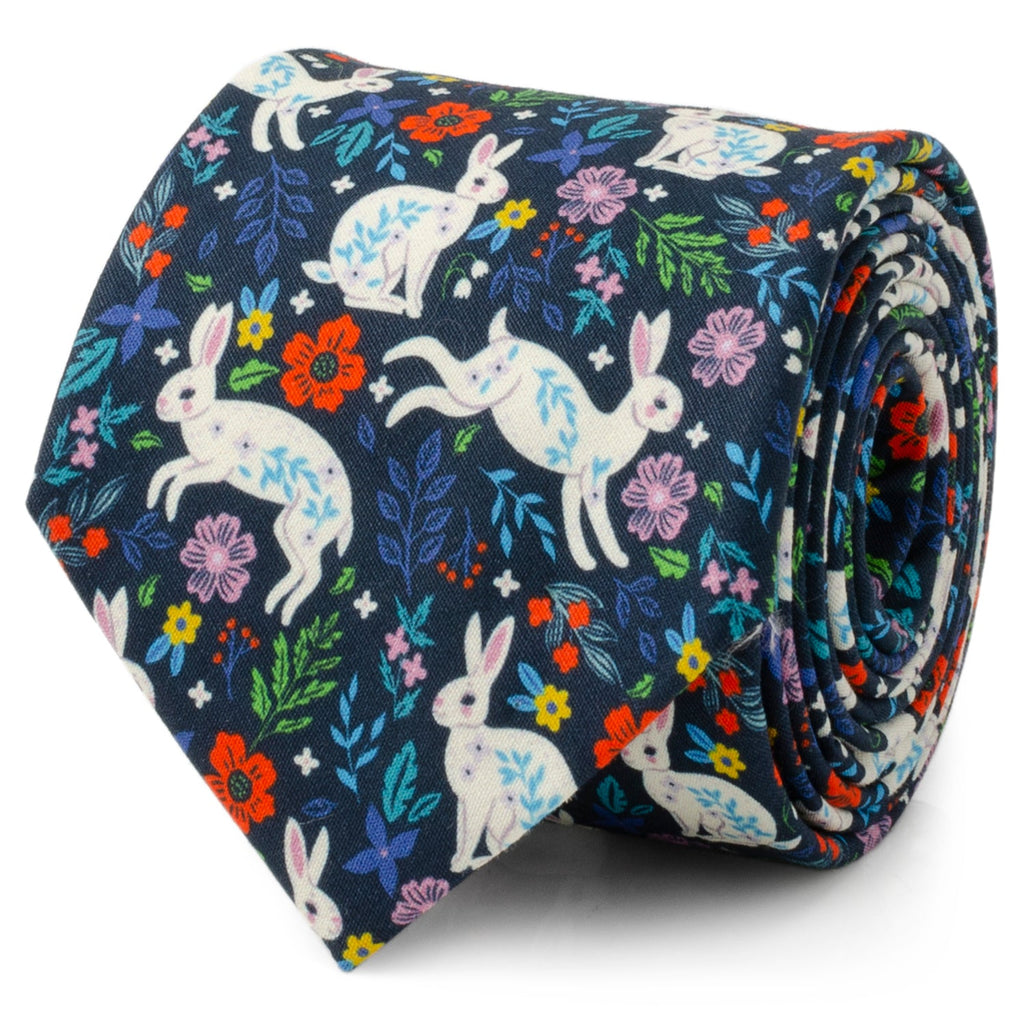 A navy blue men's necktie decorated with a white rabbit and colorful floral pattern, shown in a rolled detail shot and on a mannequin.