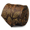 Close-up of a brown necktie with an orange printed pattern of pumpkins and leaves, tied in a knot against a white shirt and brown suit jacket.