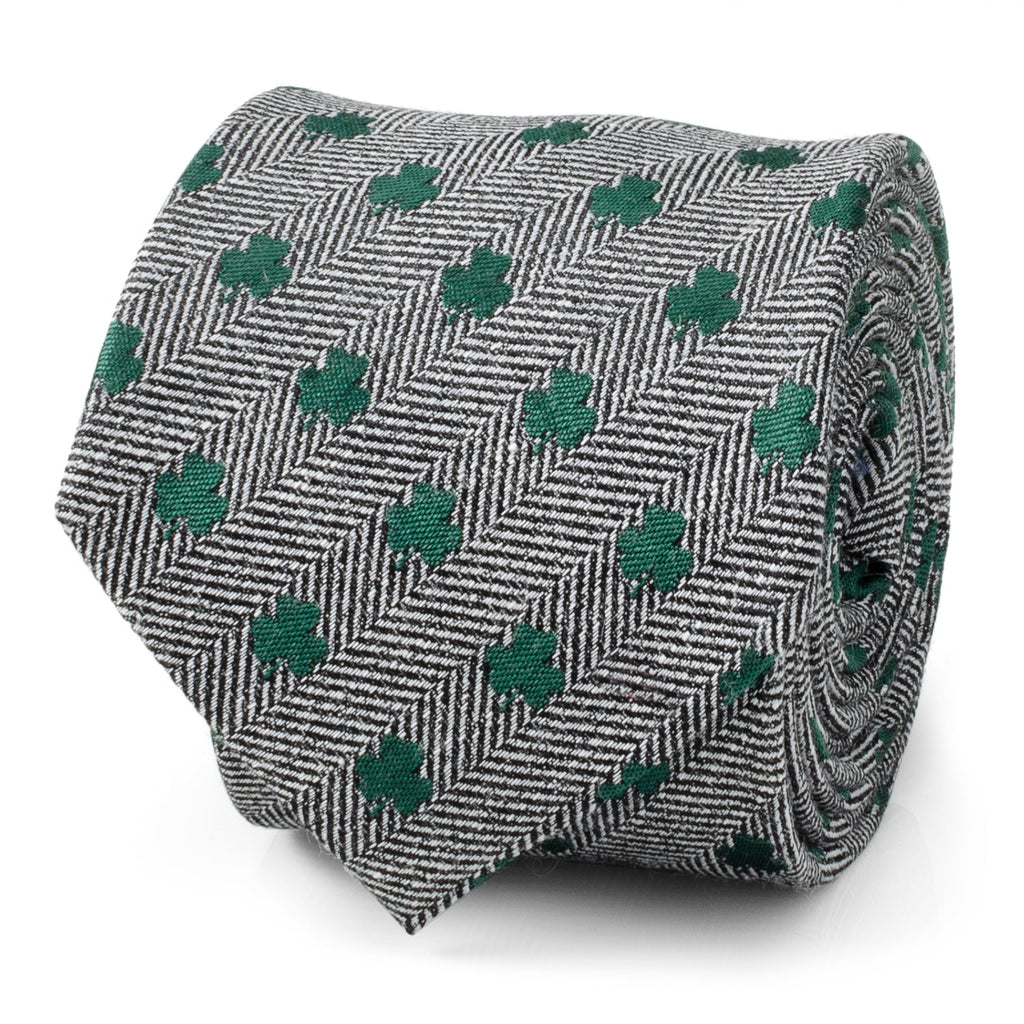 Close up and worn view of a gray herringbone necktie with small green shamrock patterns.