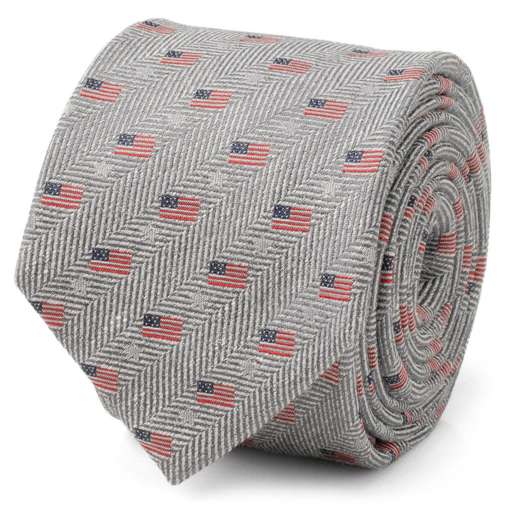 A light gray necktie featuring a herringbone pattern and small American flag prints, shown in a roll and on a mannequin.