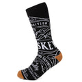A pair of black crew socks featuring white graphic whiskey-themed text and tan colored heel and toe details.