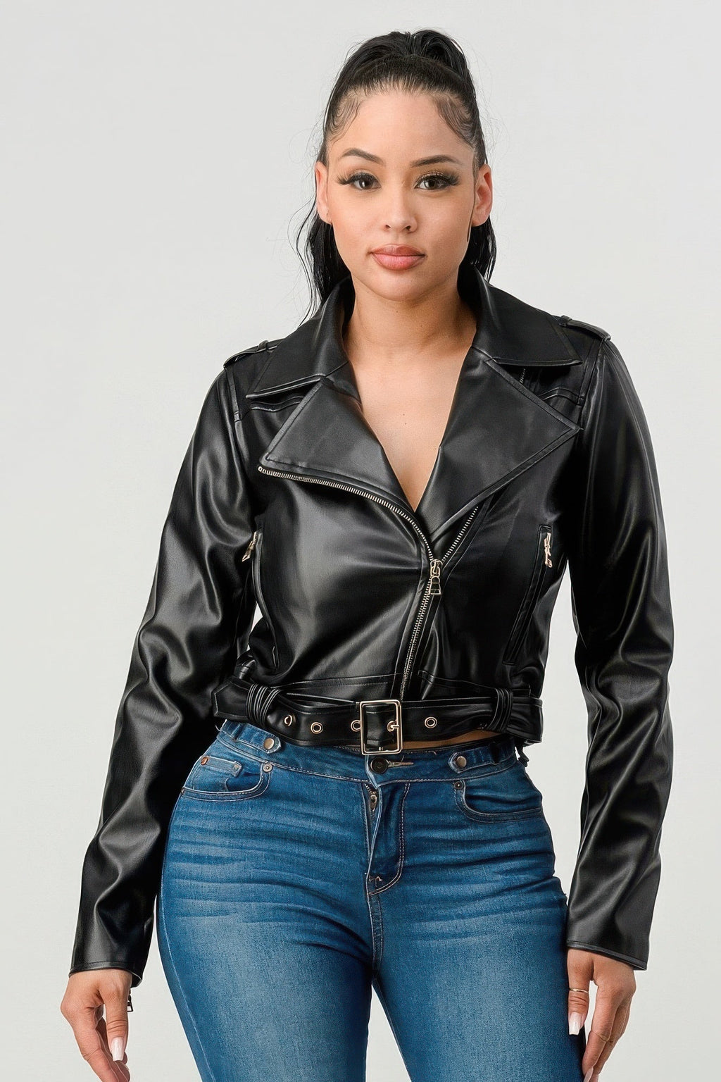 A woman wearing a fitted black PU leather moto jacket with a belt, paired with blue jeans.