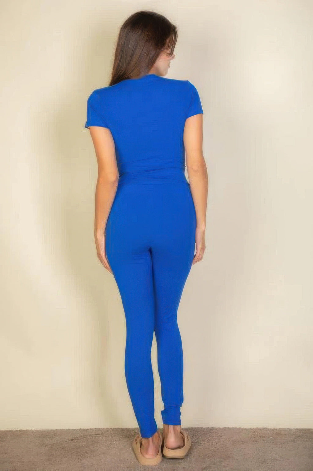 Woman wearing a blue jumpsuit against a beige wall