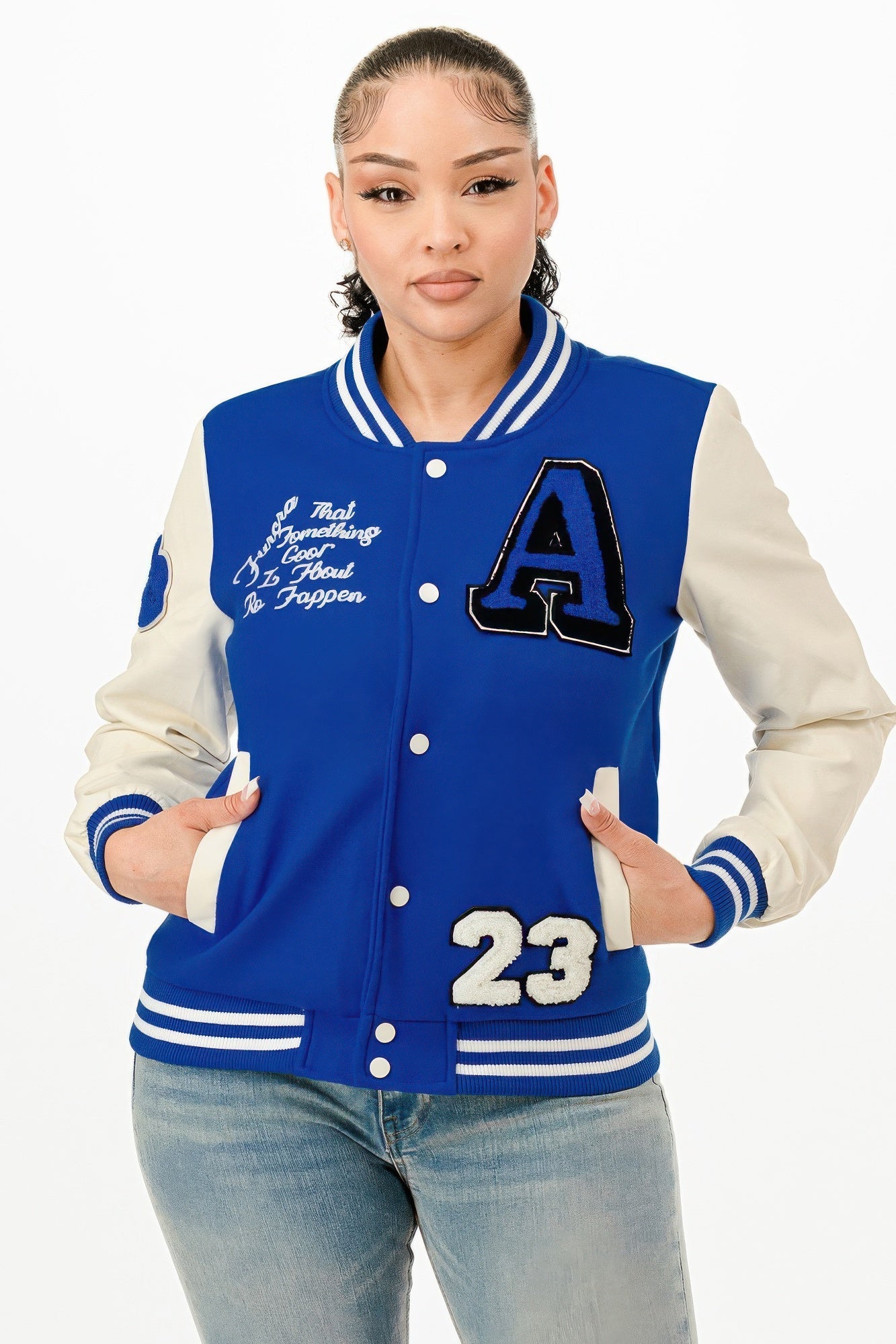 A woman wearing a royal blue varsity bomber jacket with cream sleeves and graphic patches on a white background.