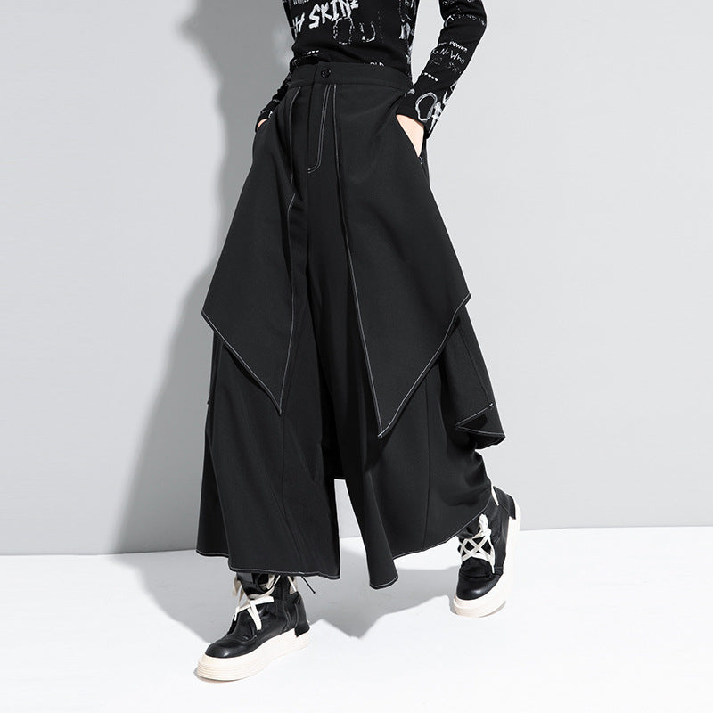 Model wearing black loose wide-leg pants with white decorative stitching, styled with a black long-sleeve top and black and white sneakers.