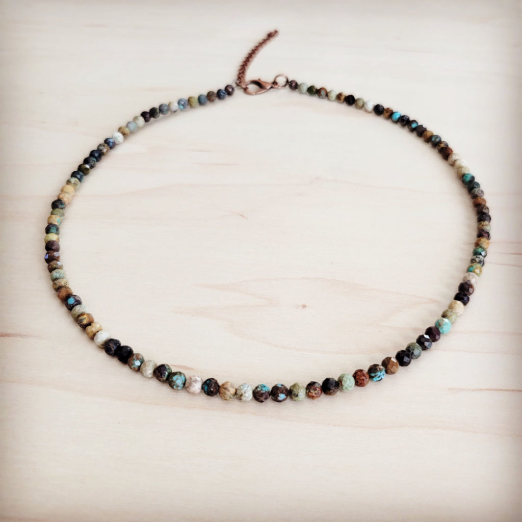 A faceted Hubei turquoise beaded collar necklace with copper-tone hardware laid flat on a wooden surface.