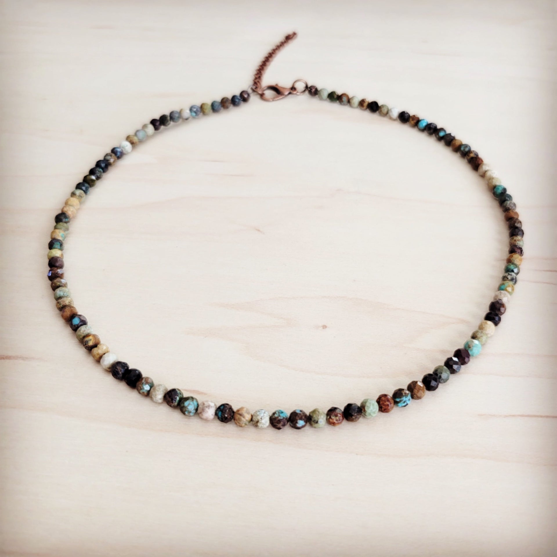 A faceted Hubei turquoise beaded collar necklace with copper-tone hardware laid flat on a wooden surface.