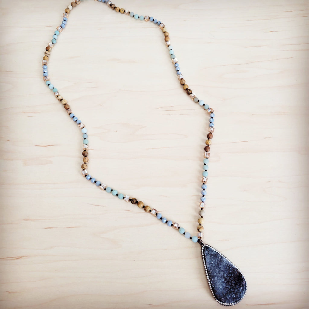 A long beaded necklace featuring blue amazonite and earth-toned beads with a large pear-shaped black druzy pendant.