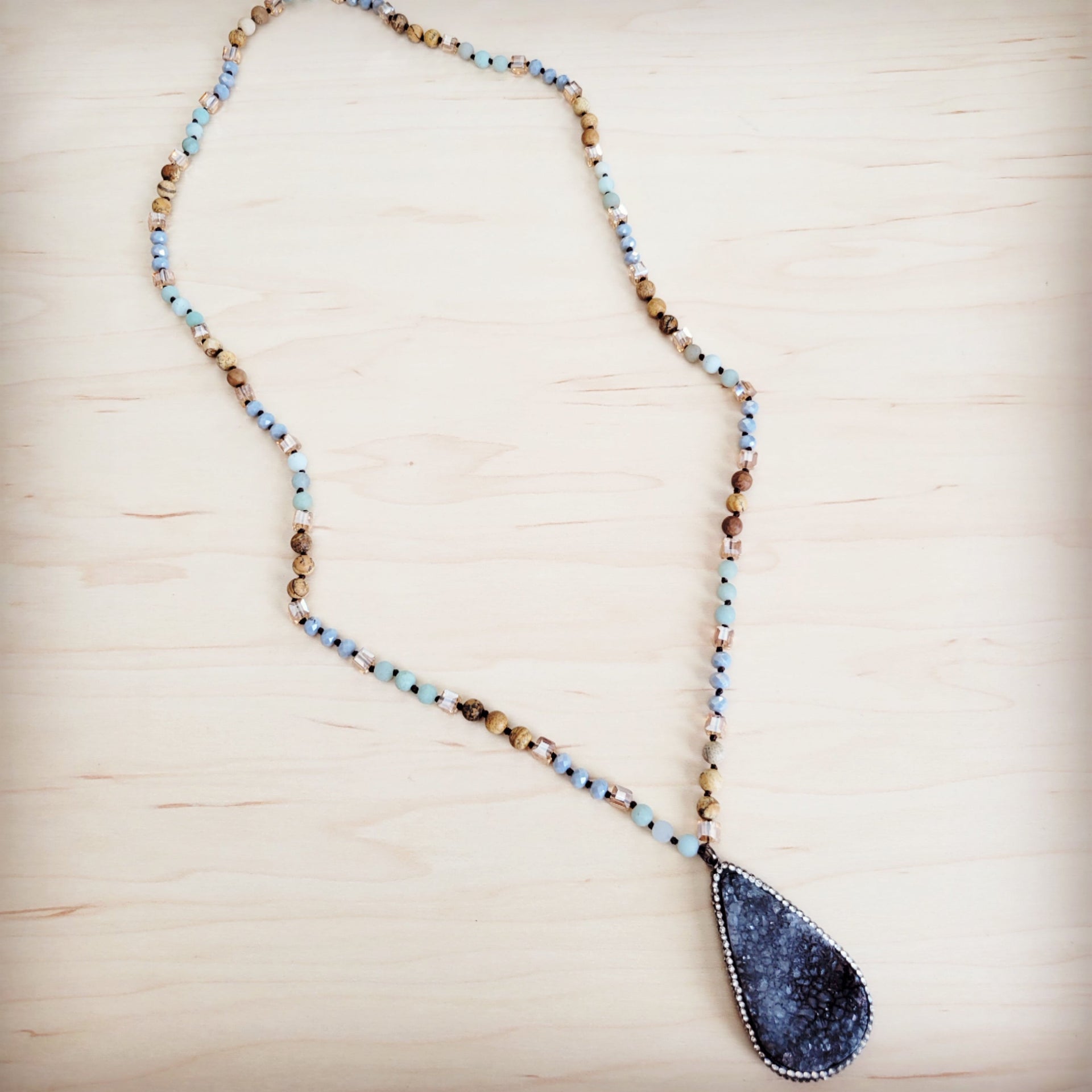 A long beaded necklace featuring blue amazonite and earth-toned beads with a large pear-shaped black druzy pendant.