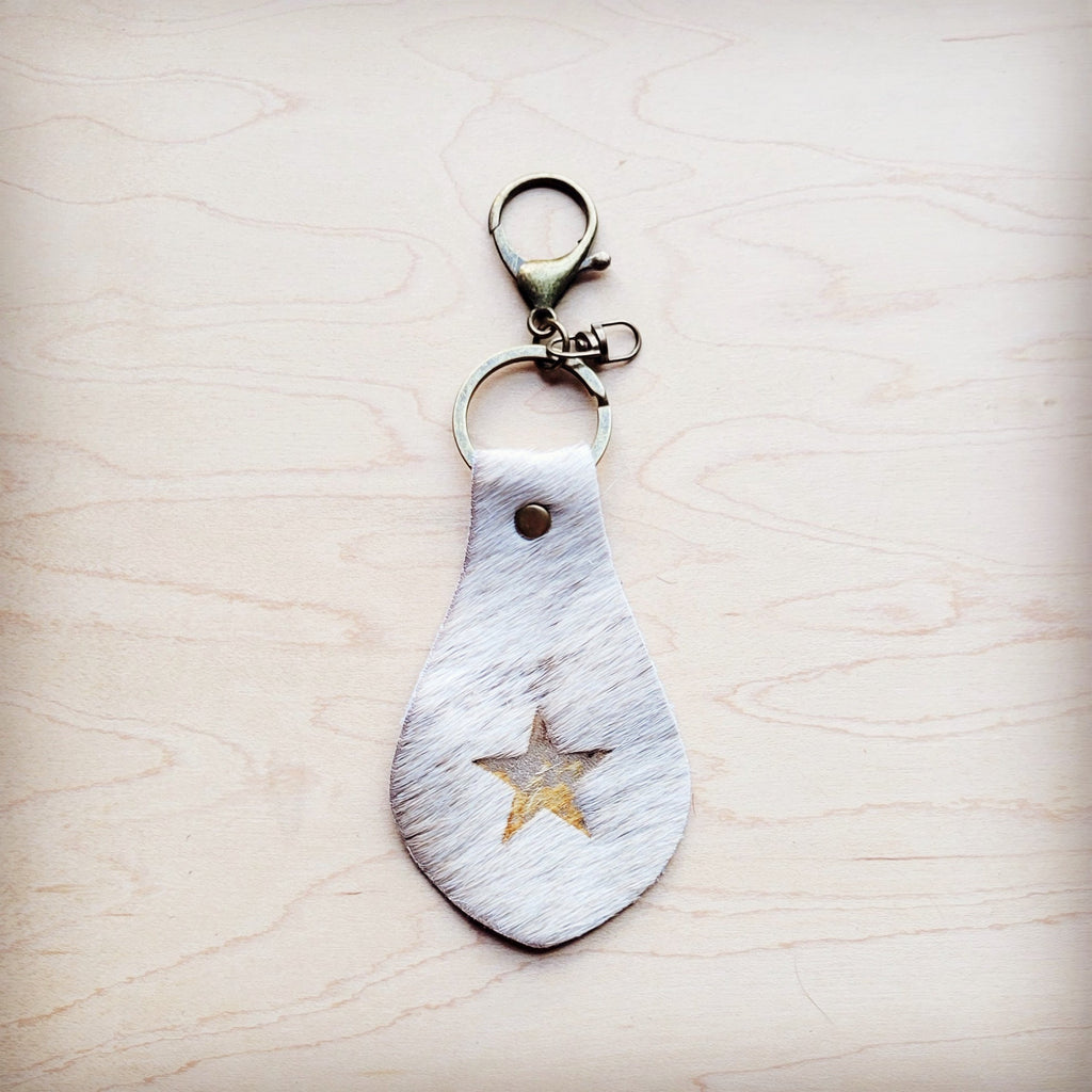 White hair-on-hide leather key chain with a star cutout featuring gold metallic underlay on a wooden surface.