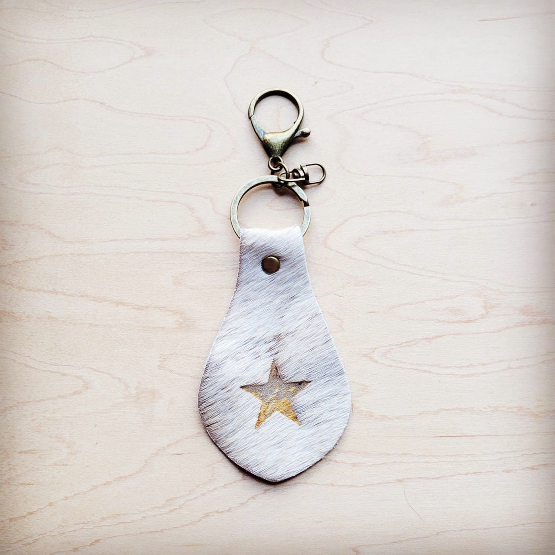 White hair-on-hide leather key chain with a star cutout featuring gold metallic underlay on a wooden surface.