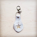 White hair-on-hide leather key chain with a star cutout featuring gold metallic underlay on a wooden surface.