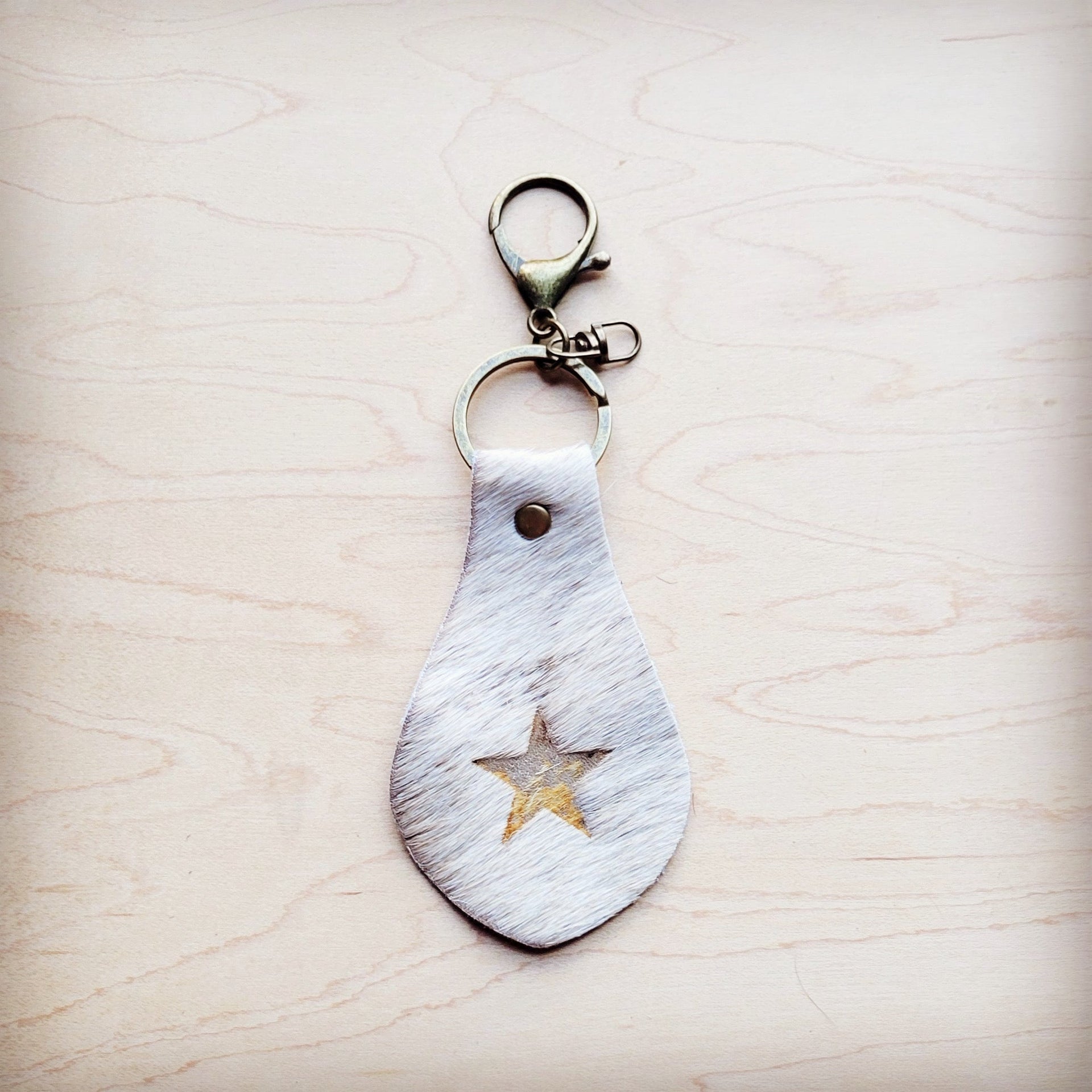 White hair-on-hide leather key chain with a star cutout featuring gold metallic underlay on a wooden surface.