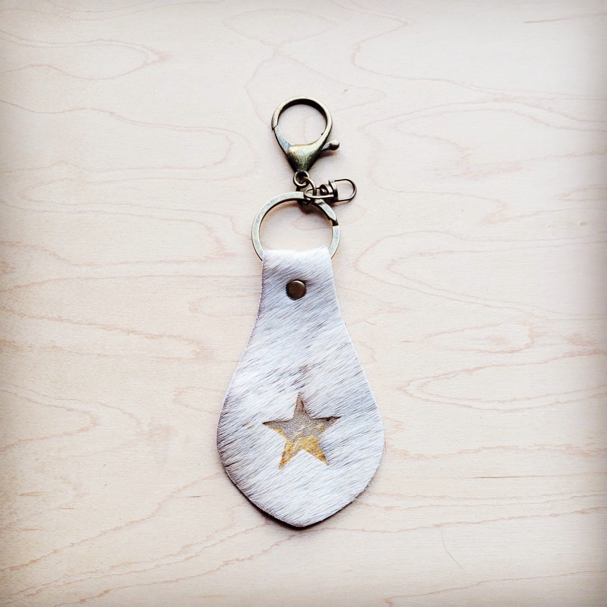 White hair-on-hide leather key chain with a star cutout featuring gold metallic underlay on a wooden surface.