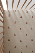 Close up and full view of a neutral striped muslin crib sheet with small brown teddy bear print inside a wooden crib.