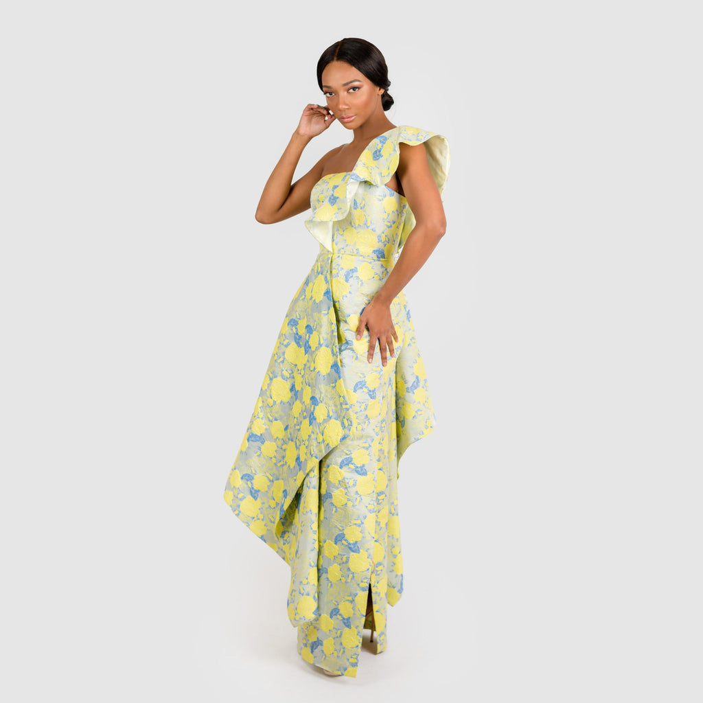 A woman modeling a yellow and blue floral jacquard one-shoulder dress with a ruffled neckline.