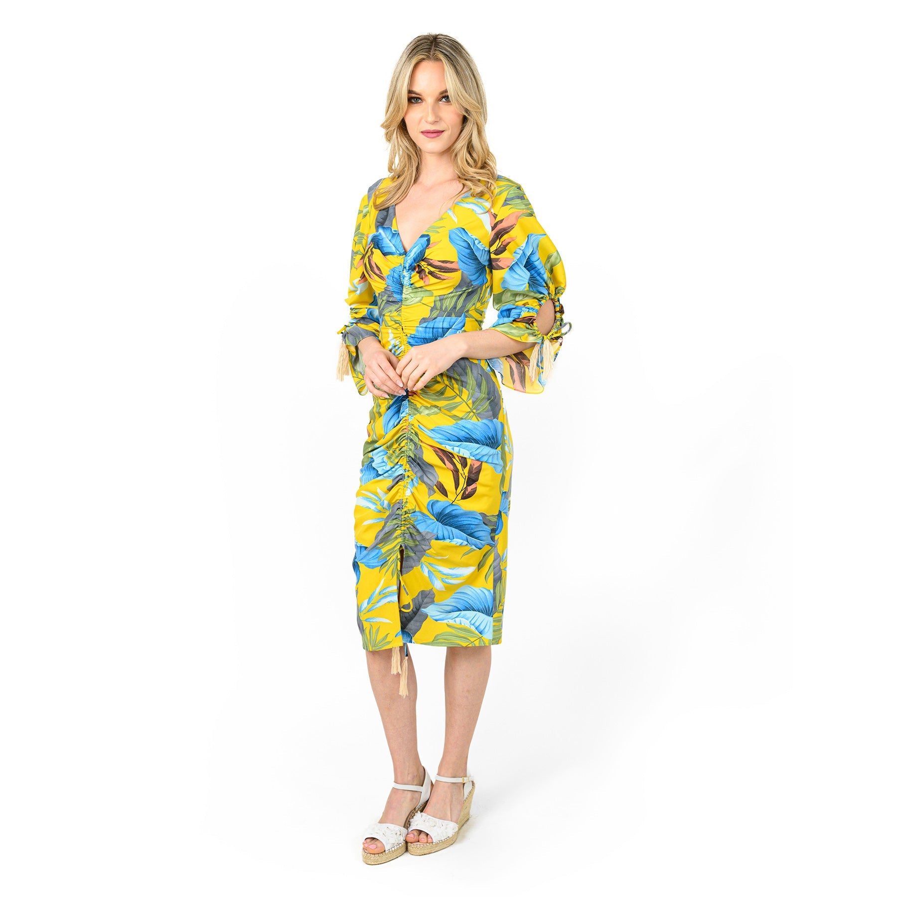 A woman wearing a bright yellow midi dress with a blue and white tropical leaf print, featuring ruched front detail and cut-out sleeves with ties.