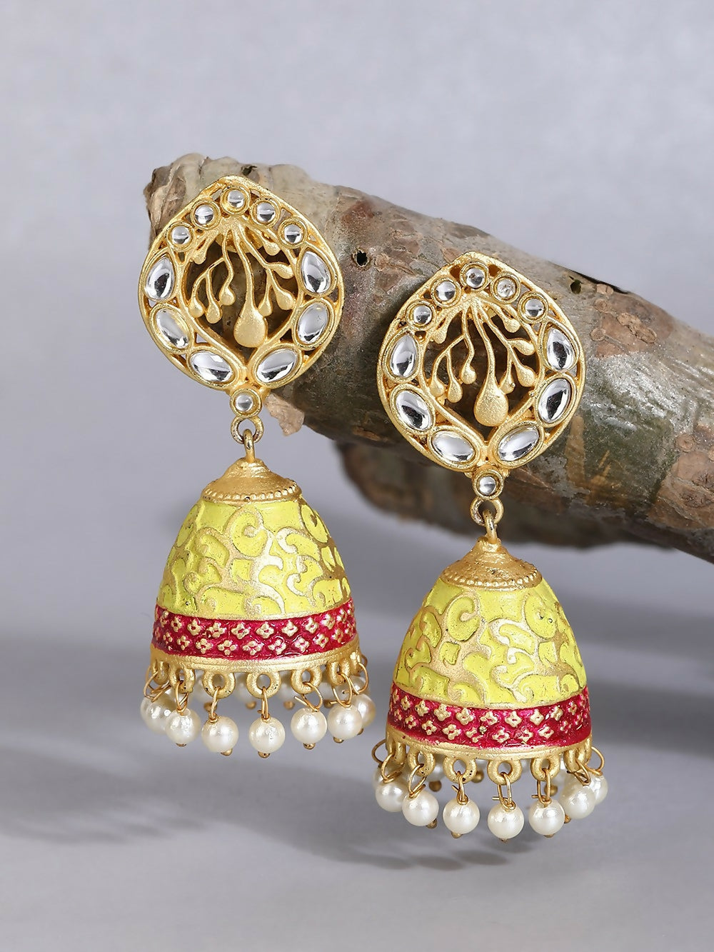 Traditional matte gold jhumka earrings adorned with white pearls and crystals, worn by a woman.