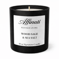A 10 oz Wood Sage and Sea Salt signature candle in a matte black jar with a minimalist label, lit and placed on a wooden surface.