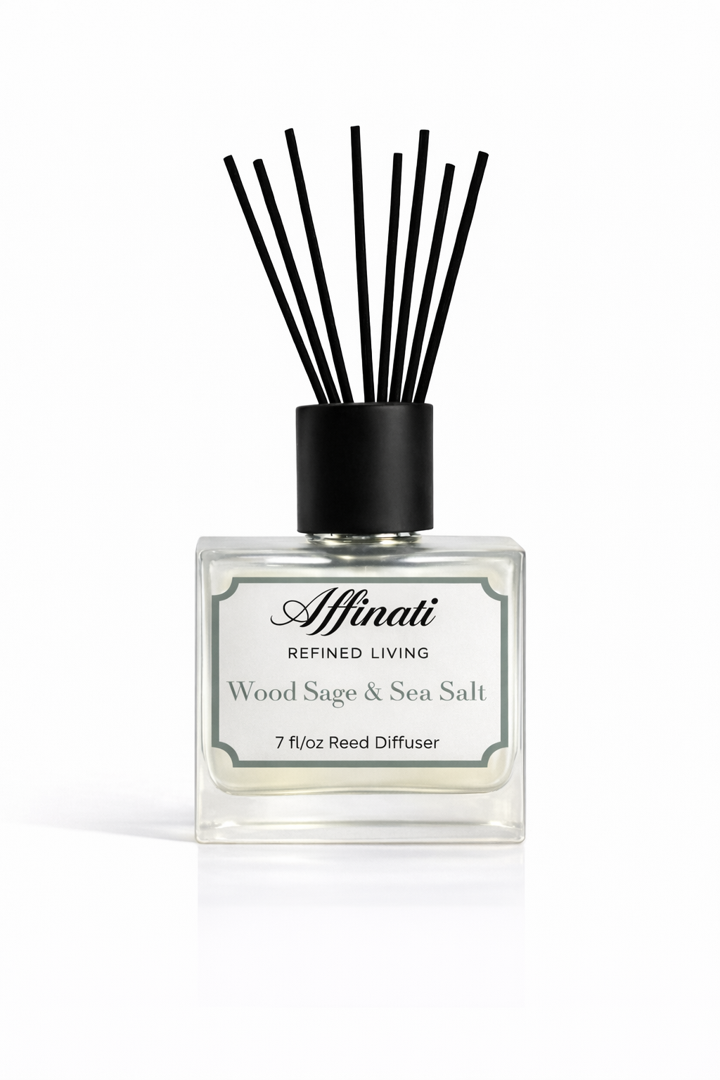 A square glass bottle of Affinati Wood Sage and Sea Salt reed diffuser with black reeds on a beach setting