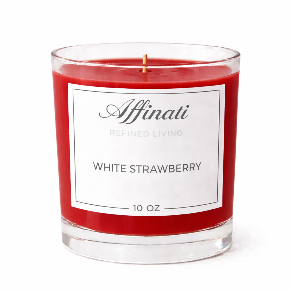 A 10 oz White Strawberry scented candle by Affinati in a clear glass jar with bright red wax, displayed on a marble surface with fresh strawberries.