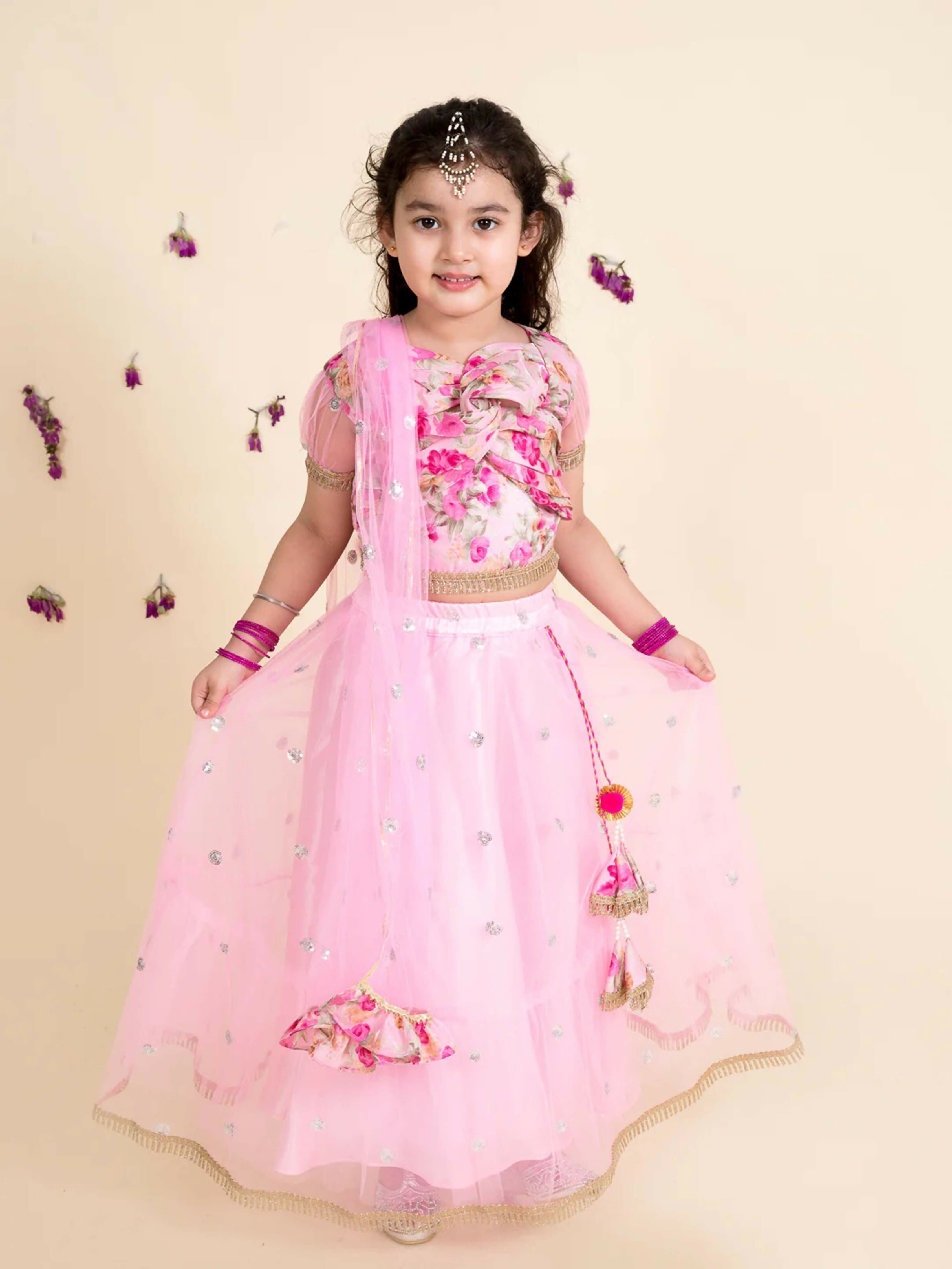 A baby girl wearing a baby pink lehenga choli set with a matching net dupatta for festive occasions.
