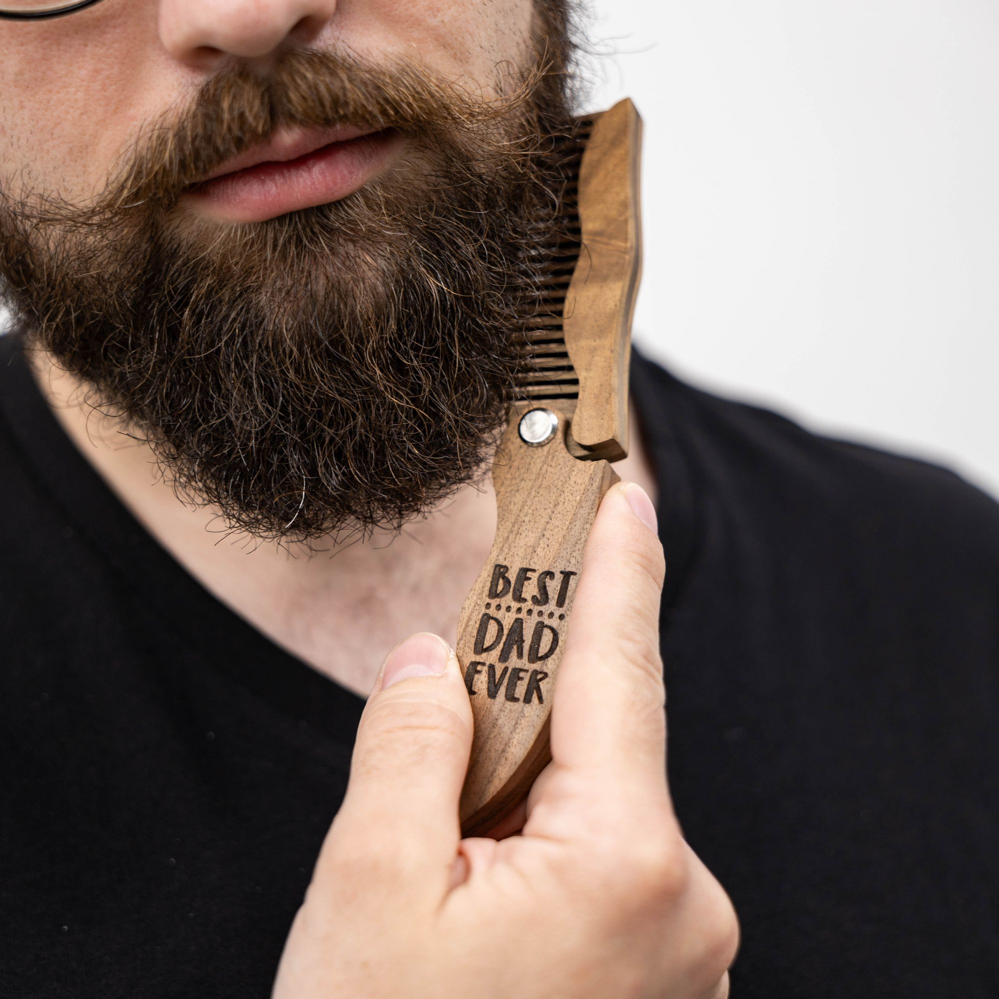 Close up of a handcrafted solid walnut wooden beard comb engraved with the text Best Dad Ever