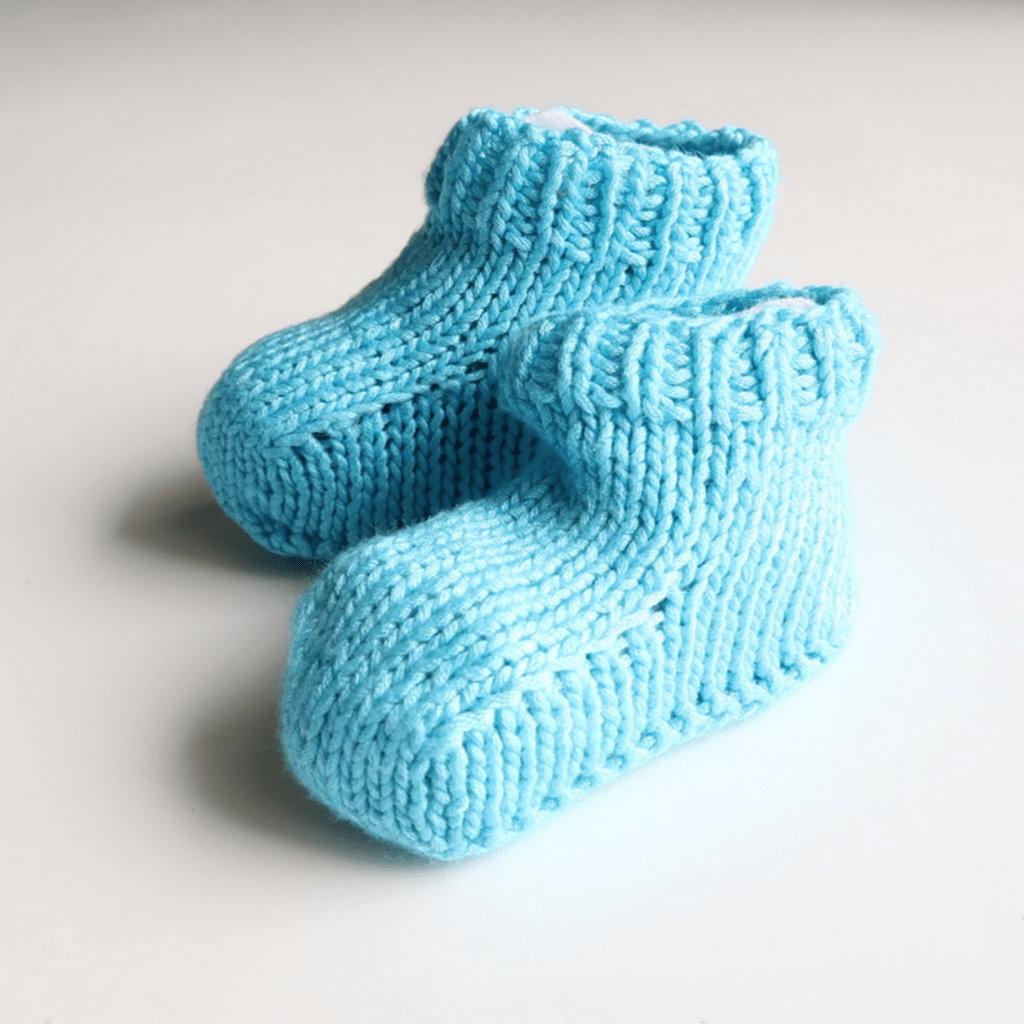 Close up of soft blue and white knitted baby booties from the Cotton Candy Knitting Kit