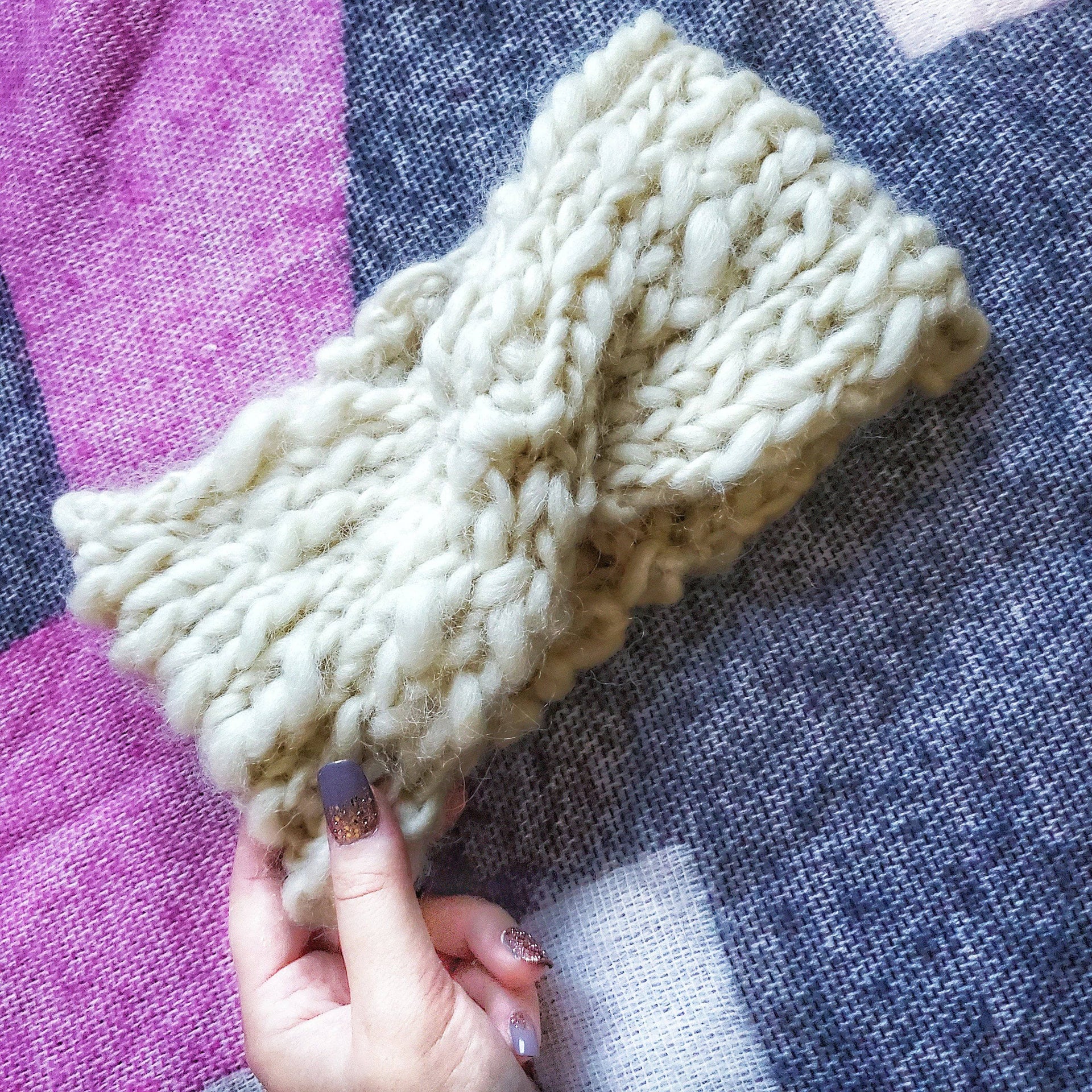 Close-up of a handmade knit headband with a central twist design on a wooden background