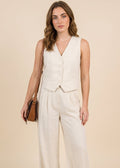 Woman wearing a white sleeveless top and wide-leg pants against a beige background