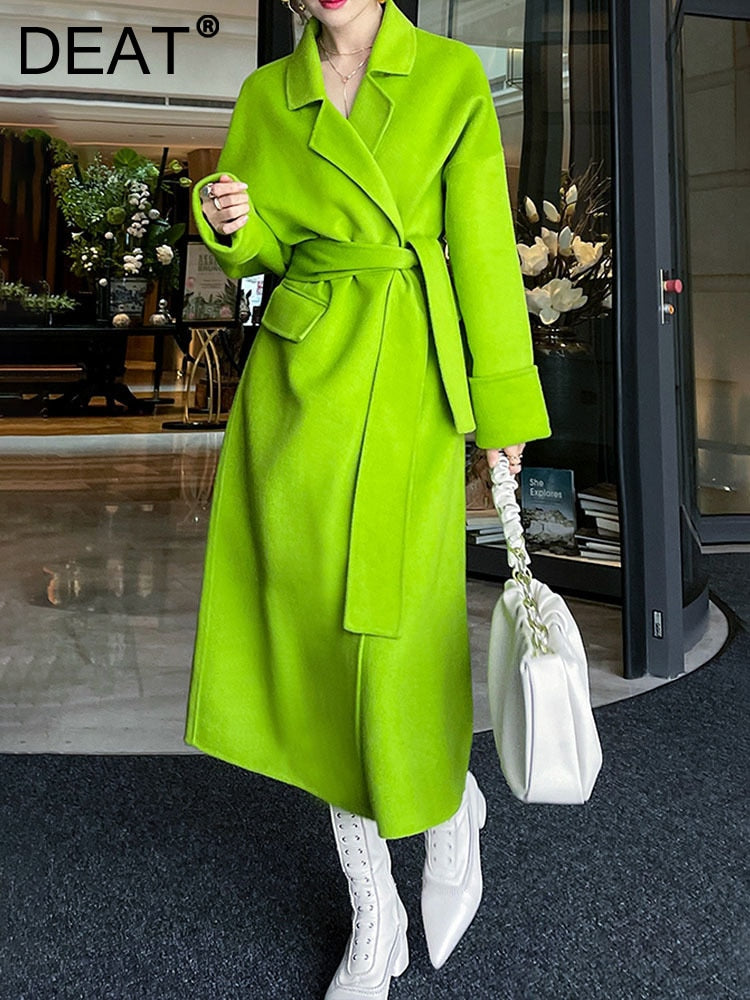 A woman models a vibrant grass green Harajuku style wool blend belted overcoat with a lapel collar, styled with white boots.