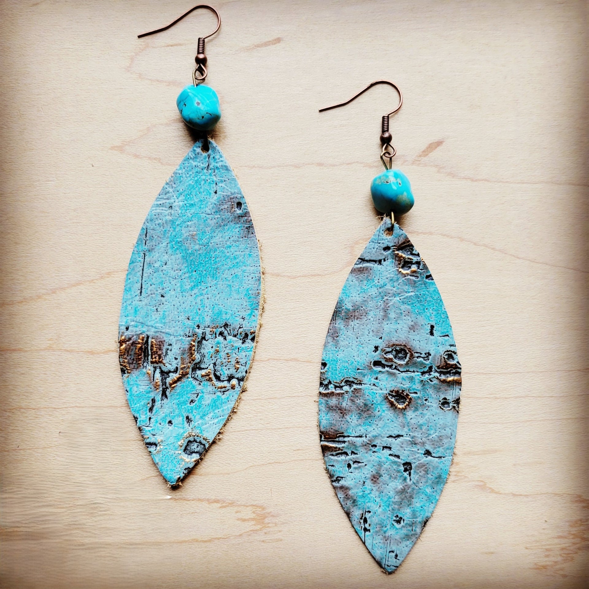 A pair of turquoise metallic leather oval earrings with a natural turquoise stone bead accent suspended from bronze-tone ear wires.