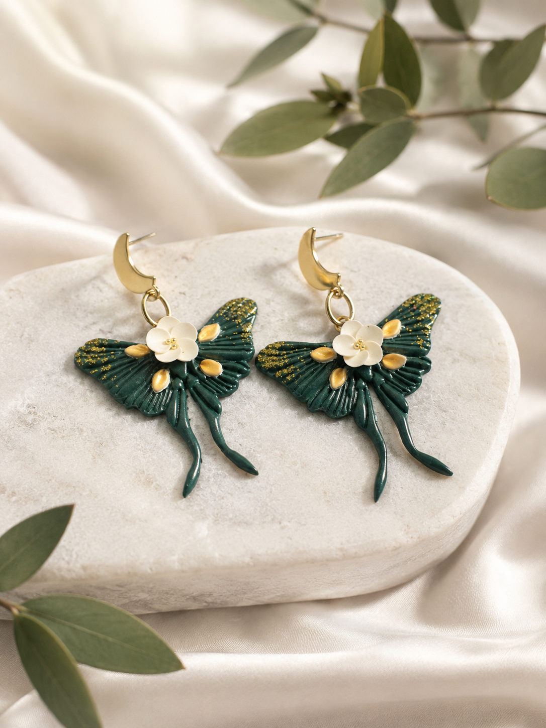 A pair of handcrafted Emerald Luna Moth earrings made from detailed polymer clay.