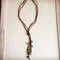 Rustic brown leather lasso necklace featuring multiple strands, a central knot, and dangling turquoise beads.