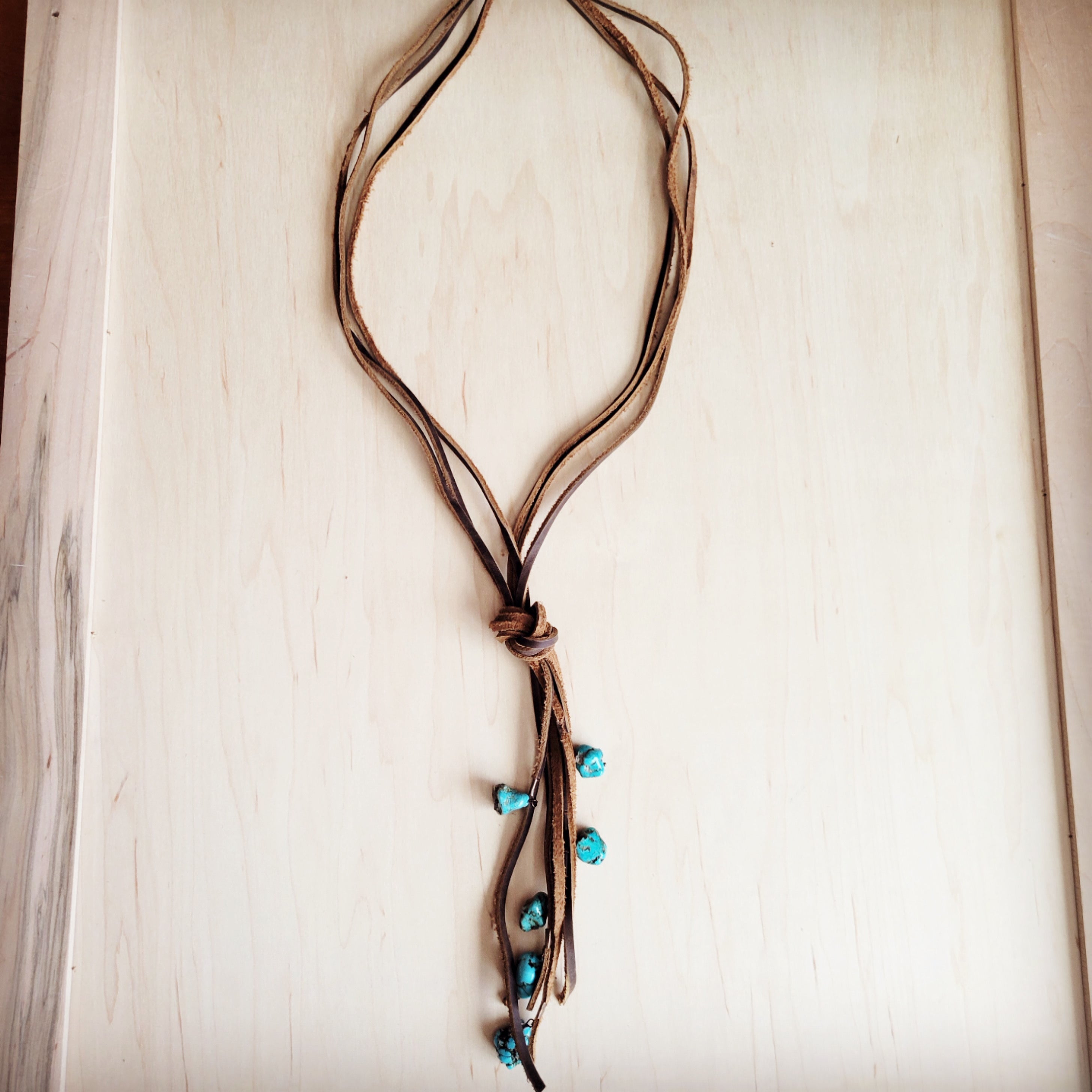 Rustic brown leather lasso necklace featuring multiple strands, a central knot, and dangling turquoise beads.
