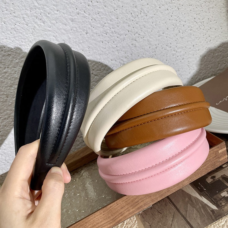Four padded PU headbands in off-white, black, brown (khaki), and pink, stacked neatly on a wooden tray.