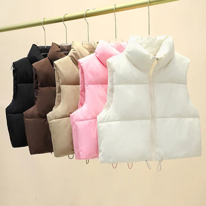 A row of five Harajuku style cropped puffer vests in off-white, black, coffee, khaki, and rose red, hanging on a rail with a stand-up collar and full zipper.